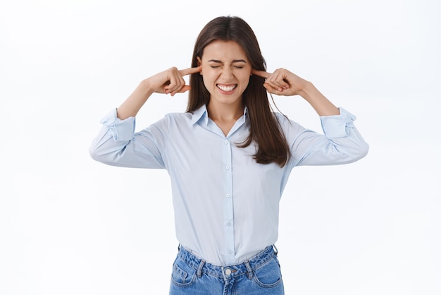 Arrêtez ce bruit ennuyeux désagréable Femme ressentant un énorme inconfort gêné par la musique forte jouée chez les voisins fermez les oreilles avec les doigts fermez les yeux et grimacez irrité fond blanc