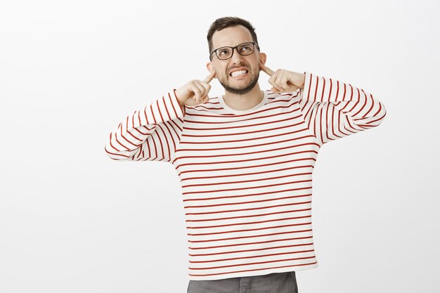 Arrêtez ce bruit. Portrait d'un homme de race blanche énervé en colère dans des lunettes noires, couvrant les oreilles avec l'index et grimaçant de colère