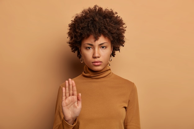 Arrêtez ici. Femme sérieuse à la peau sombre se tient avec la main tendue, fait un geste d'interdiction, interdit quelque chose, sourit narquoisement