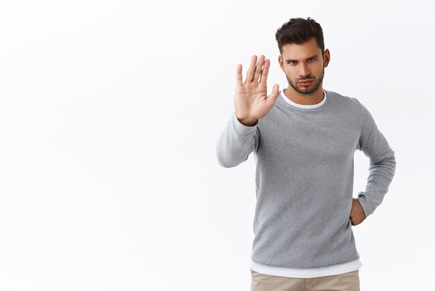 Arrêtez-vous ici Guy disant non regarder sérieusement la caméra sous le front lever la main dans l'interdiction ne pas ou interdire le geste donner l'avertissement et la désapprobation de l'action debout fond blanc