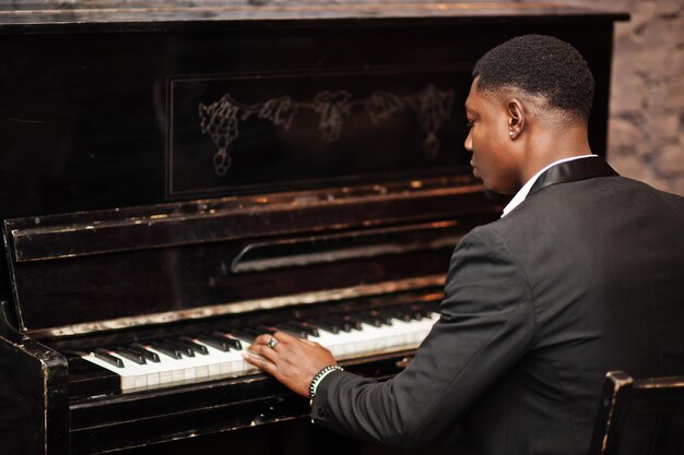 L'arrière d'un homme afro-américain fort et puissant en costume noir joue du piano