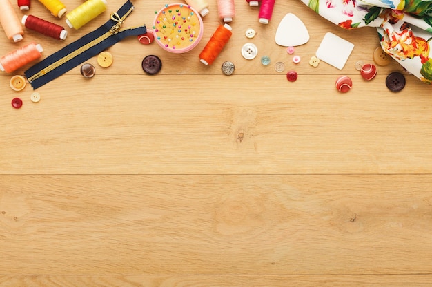 Arrière-plan de couture créative, vue de dessus. collection de divers boutons, fils et épingles disposés en bordure sur une table en bois, espace de copie.