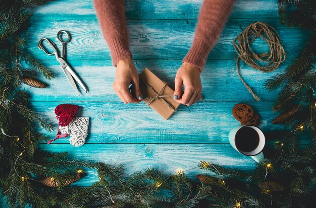 Articles de Noël sur une table en bois bleue. Mains de la femme enveloppant le cadeau de Noël.