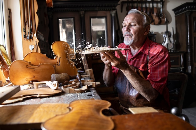 Artisan charpentier senior travaillant avec du bois franc en atelier et soufflant de la sciure de bois