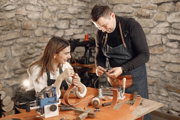 Photo gratuite artisan mature avec jeune femme travaillant dans l'espace de travail homme et femme portant un tablier et faisant une ceinture fond de texture de pierre sombre grounge