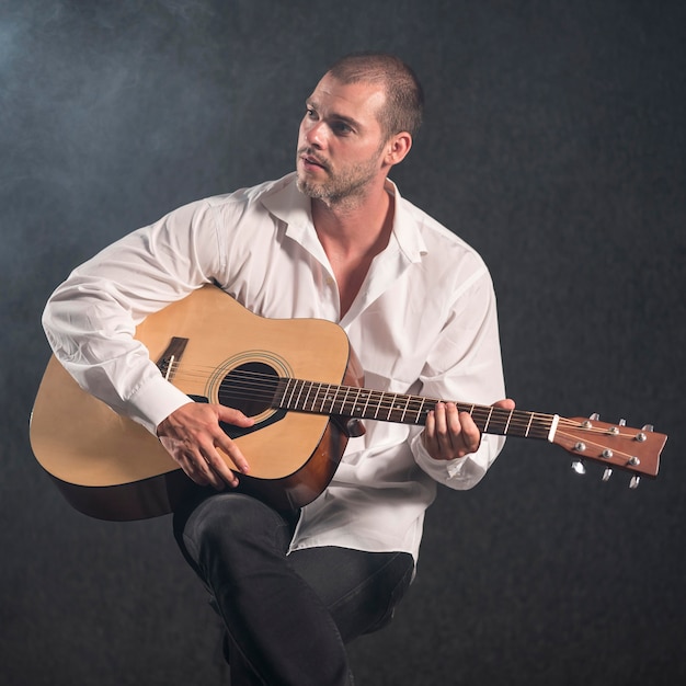 Photo gratuite artiste en chemise blanche jouant de la guitare et regardant ailleurs