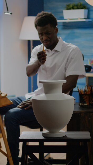Artiste d'ethnie afro-américaine analysant un vase pour un dessin créatif assis dans un atelier. Adulte noir avec imagination artistique utilisant l'inspiration pour un chef-d'œuvre réussi