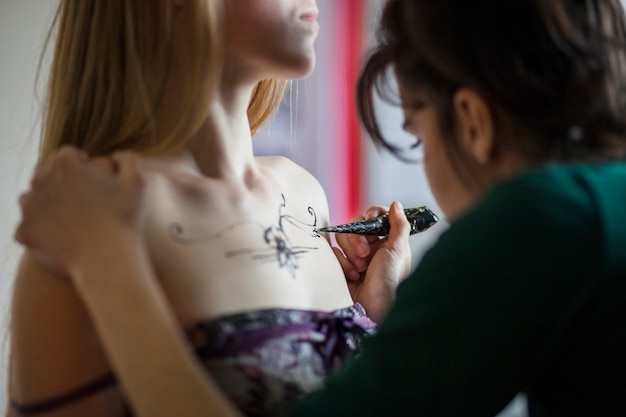 Un artiste féminin mehndi dessinant un tatouage sur la poitrine de la femme