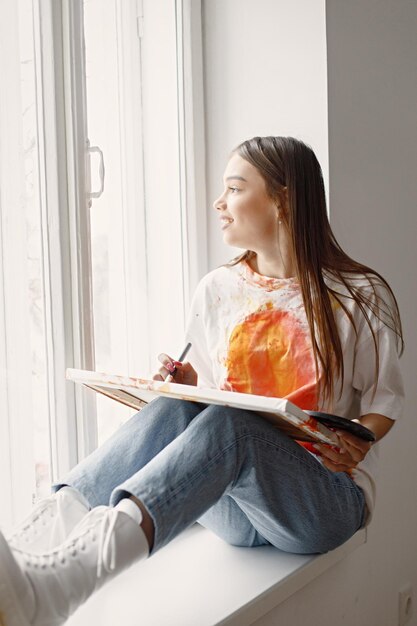 Artiste féminine assise sur un rebord de fenêtre tenant une toile et des pinceaux