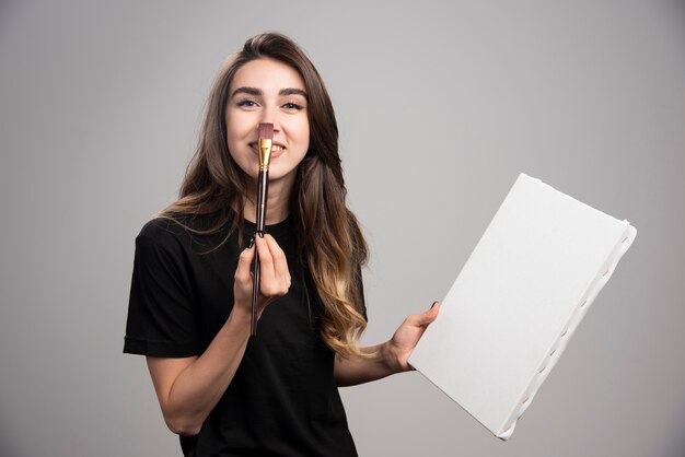 Artiste féminine en chemise noire touchant son nez avec un pinceau.