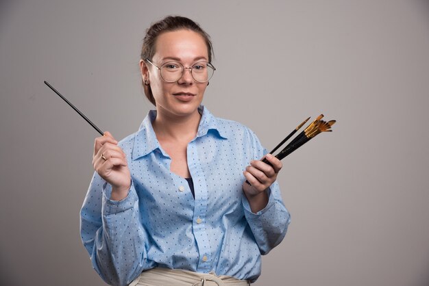 Artiste femme détient des pinceaux sur fond gris. Photo de haute qualité