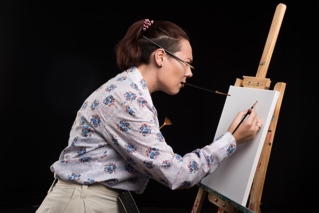 L'artiste de femme peint une image sur la toile avec la brosse sur le noir