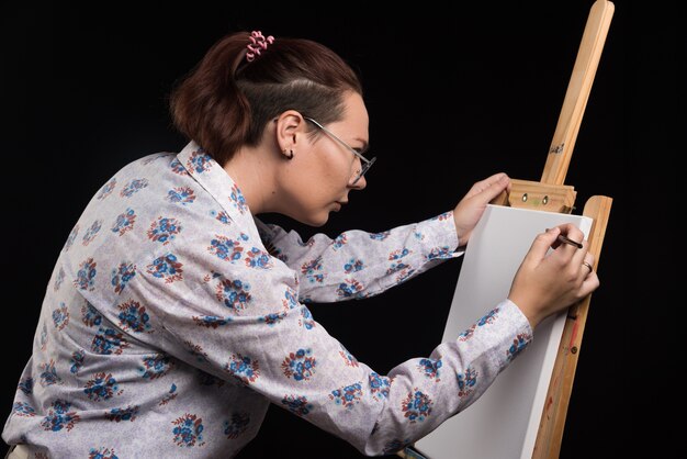 Artiste femme peint une image sur toile avec un crayon sur fond noir