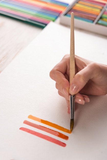 Artiste peignant des rayures colorées au pinceau sur papier blanc