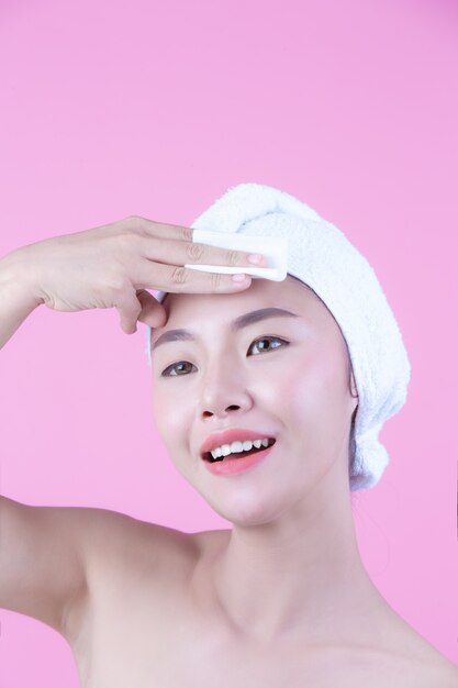 Asiatique belle femme essuyant le visage sur un fond rose, cosmétologie et spa.