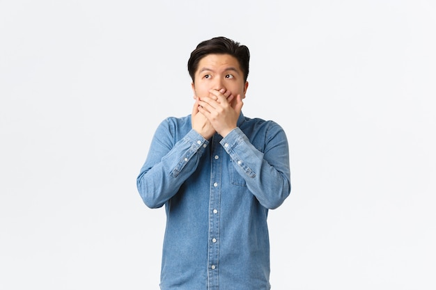 Un Asiatique Choqué Et Sans Voix Est Témoin De Quelque Chose, Couvre La Bouche Avec Les Mains Et Regarde Dans Le Coin Supérieur Gauche, Haletant Stupéfait Par La Révélation, Entend Des Potins époustouflants, Fond Blanc.