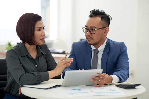 Photo gratuite asiatique homme et femme en tenue professionnelle assis à l'intérieur avec tablette et parler