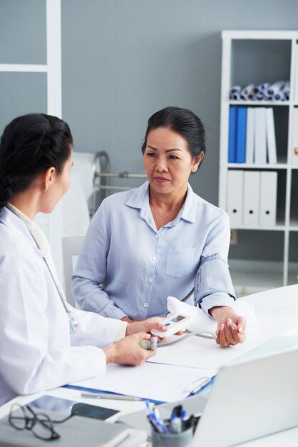 Asiatique mature assise dans le bureau du médecin et ayant une pression artérielle mesurée