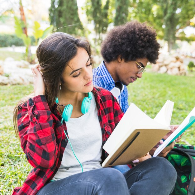 Assez détendue jeune femme lisant un livre avec son ami à la pelouse