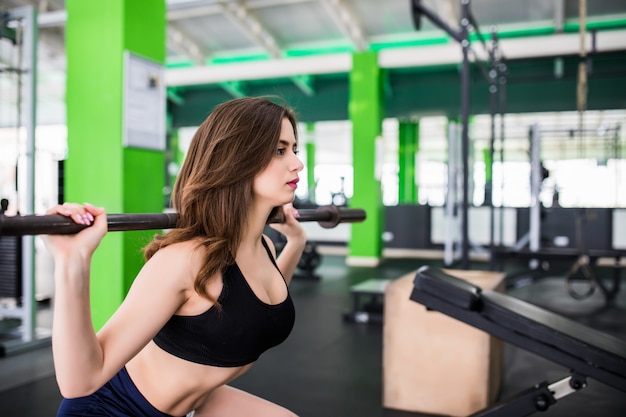 Assez forte jeune femme faisant des exercices accroupis avec haltères habillés en vêtements de sport de mode dans sportclub