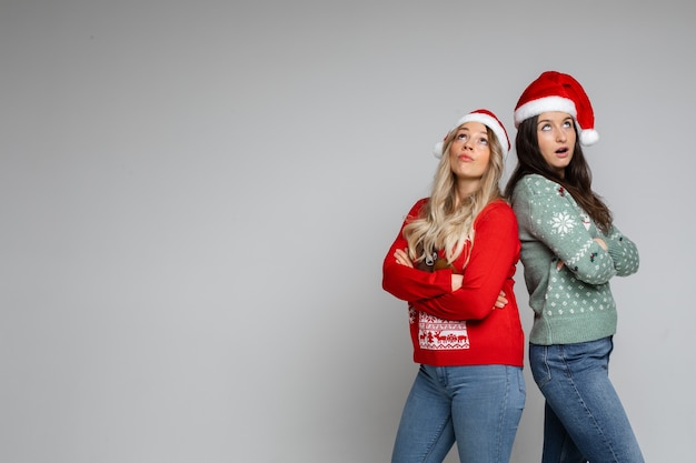 Assez surpris jeunes filles de Noël en bonnets de Noel et chandails d'hiver posant sur fond gris studio avec espace de copie