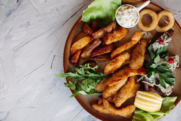 Assiette d'argile pleine d'apéritifs servis avec des pépites de poulet dorées cuites avec une croûte croustillante de délicieux canapés avec du hareng et des tomates cerises sauce à l'ail décorées de salade fraîche et de fromage