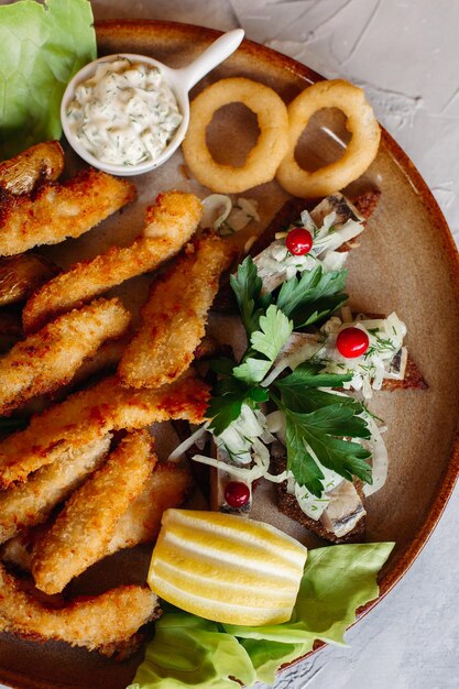 Assiette d'argile pleine d'apéritifs servis avec des pépites de poulet dorées cuites avec une croûte croustillante de délicieux canapés avec du hareng et des tomates cerises sauce à l'ail décorées de salade fraîche et de fromage