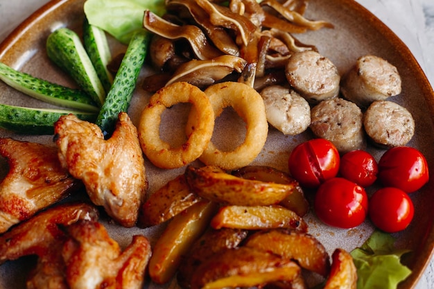 Assiette d'argile pleine d'apéritifs servis avec des pépites de poulet dorées cuites avec une croûte croustillante de délicieux canapés avec du hareng et des tomates cerises sauce à l'ail décorées de salade fraîche et de fromage