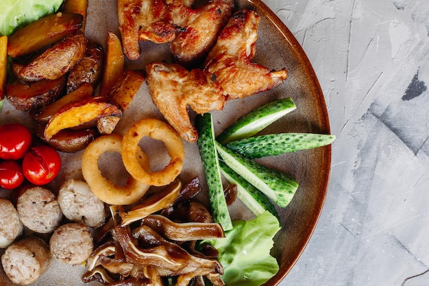 Assiette d'argile pleine d'apéritifs servis avec des pépites de poulet dorées cuites avec une croûte croustillante de délicieux canapés avec du hareng et des tomates cerises sauce à l'ail décorées de salade fraîche et de fromage