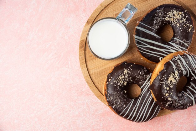 Assiette de beignets au chocolat avec un verre de lait sur fond rose.