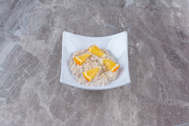 Une assiette blanche avec de la bouillie d'avoine saine et des tranches de fruits orange.