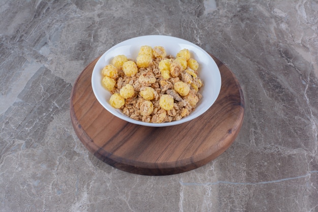 Une assiette blanche de cornflakes sains sur une planche ronde en bois.