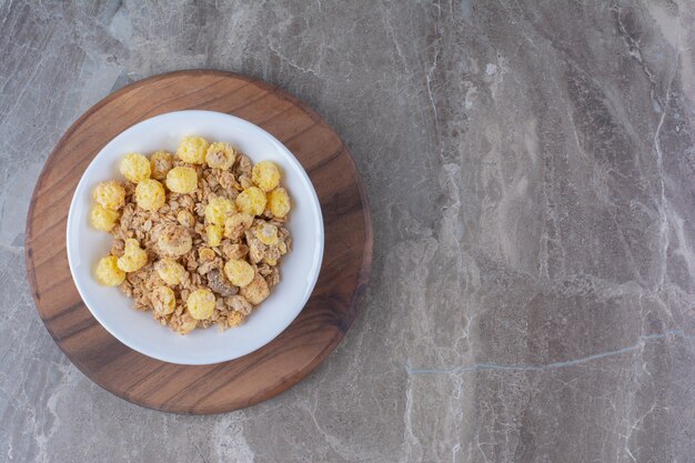 Une assiette blanche de cornflakes sains sur une planche ronde en bois.