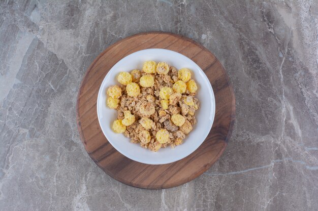 Une assiette blanche de cornflakes sains sur une planche ronde en bois.