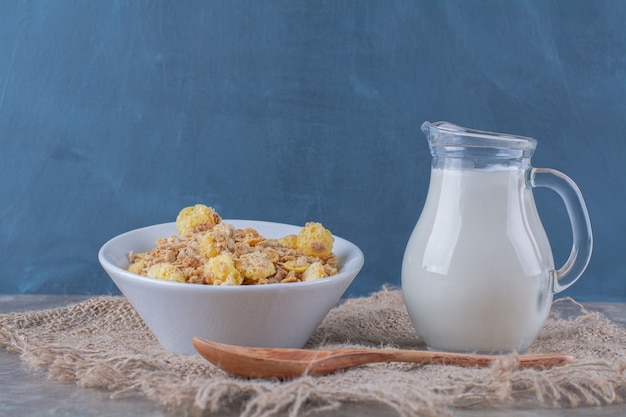 Photo gratuite une assiette blanche de cornflakes sucrés sains avec un pot de lait en verre sur un sac .