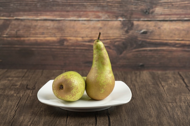 Assiette blanche de délicieuses poires mûres sur une surface en bois