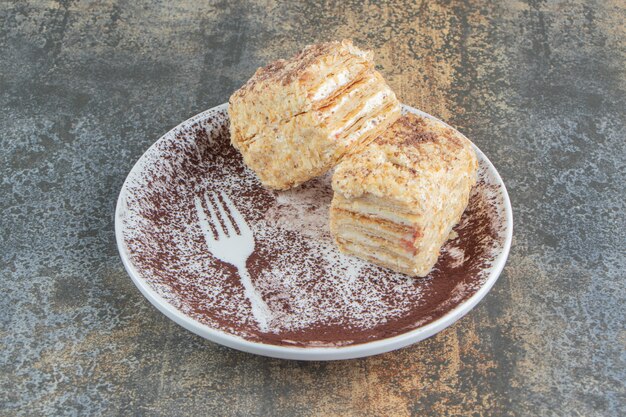 Une assiette blanche avec deux morceaux de gâteau Napoléon et de la poudre de cacao