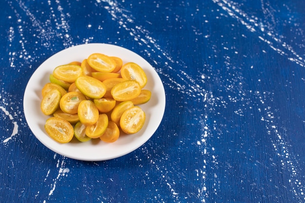 Assiette blanche de fruits kumquat tranchés sur une surface en marbre