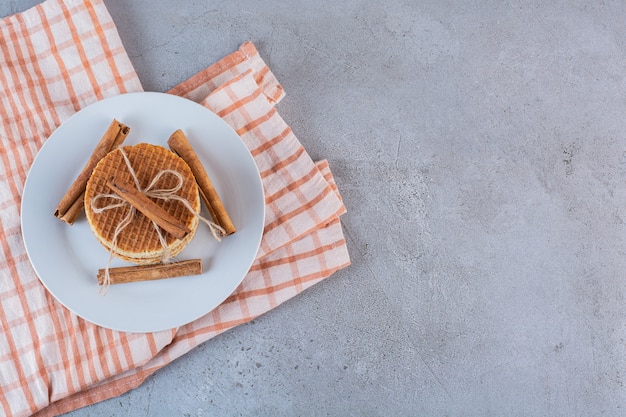 Une assiette blanche de gaufres sucrées en corde avec des bâtons de cannelle sur une surface en pierre