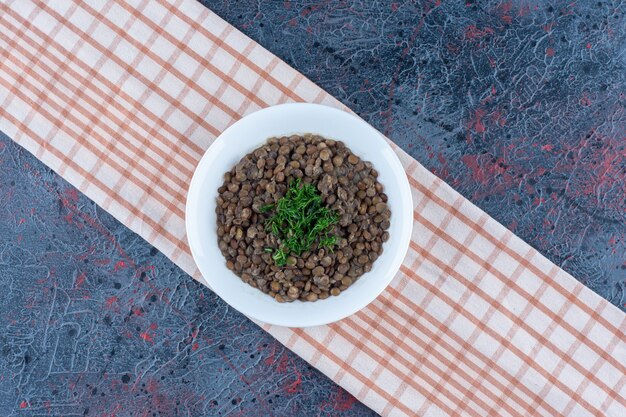 Une assiette blanche avec des haricots et des herbes sur une nappe.