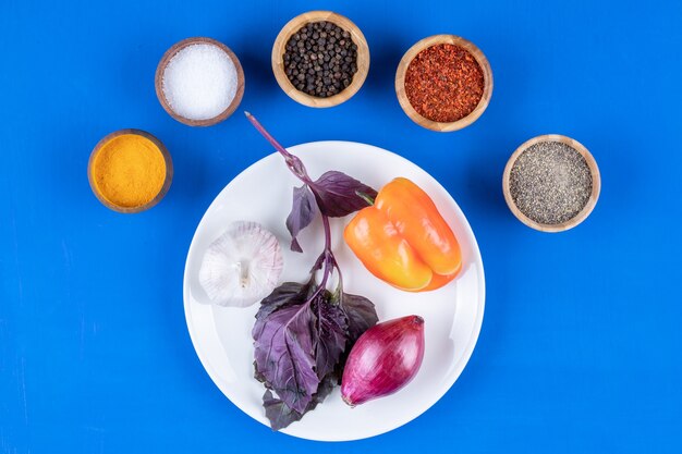 Assiette blanche de légumes frais et d'épices sur une surface bleue