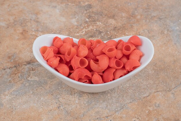 Une assiette blanche de macaronis rouges non cuits sur un espace en marbre.