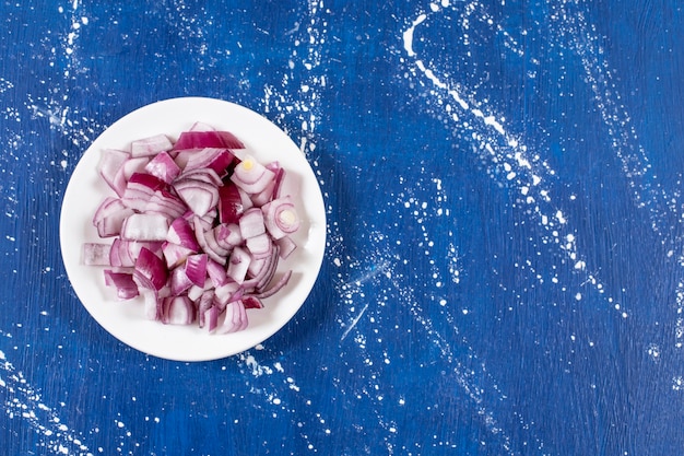 Photo gratuite assiette blanche d'oignons violets tranchés sur une surface en marbre.