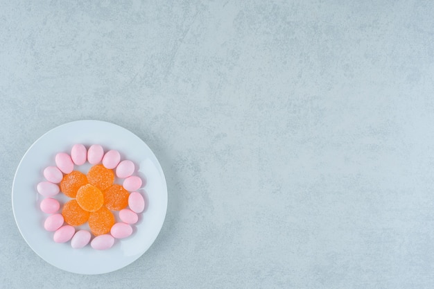 Une assiette blanche pleine de bonbons à la gelée d'orange douce et de bonbons roses