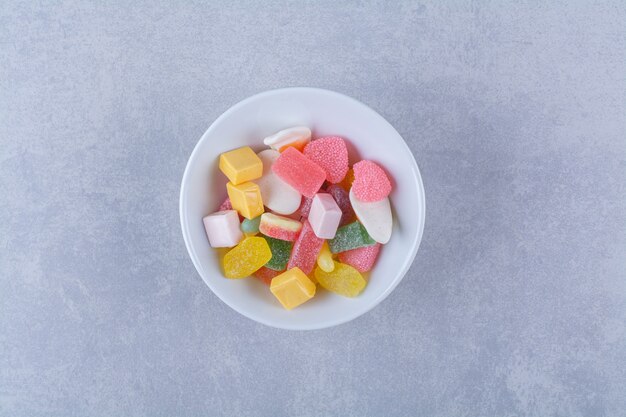 Une assiette blanche pleine de bonbons à la gelée sucrée sur une surface grise