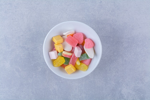 Une assiette blanche pleine de bonbons à la gelée sucrée sur une surface grise