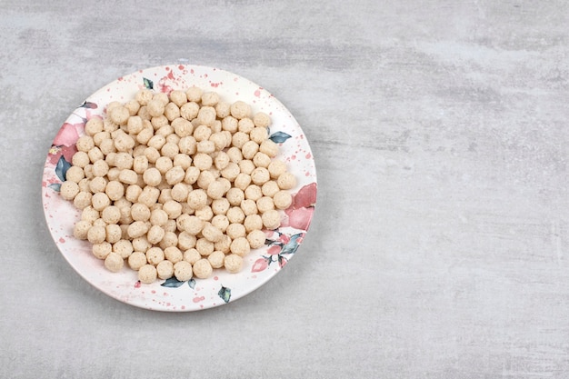 Assiette blanche pleine de boules de céréales de maïs sur table en pierre.