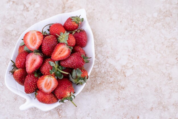 Une assiette blanche pleine de fraises sur fond de marbre.