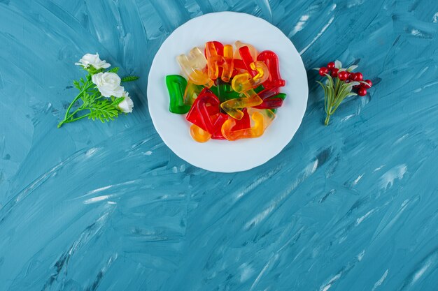 Une assiette blanche pleine de lettres en forme de confitures sucrées colorées sur fond bleu.