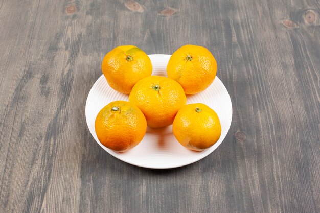 Une assiette blanche pleine de mandarines fraîches et sucrées. Photo de haute qualité